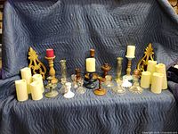 Set of candle holders, wall sconces and battery operated candles arranged on a blue moving blanket, showing various styles and materials.