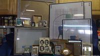 Multiple picture frames of varying sizes and styles arranged on table and against wall, including metal and plastic frames in various finishes.