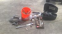 Wide view of assorted tools including a bucket of hand tools, bike lock cable, and chainsaw case open with tools inside.
