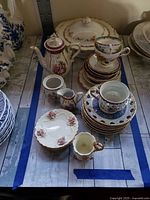 Top view of miscellaneous China items arranged on table including teapot, cups, plates, creamers, and a covered serving dish.