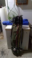 Fishing rods with reels and protective green carrying case bag, leaning on freezer