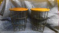 Pair of wire basket storage tables with wooden tops placed side by side on a padded blue moving blanket, showing front view of both wire baskets and wooden lids.