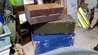 Overall view of stacked wooden toolbox and trunks showing their condition and size.