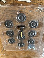 Photo showing dark colored oil rubbed bronze cabinet knobs arranged in plastic packaging with one knob upright to show side profile including screw part.