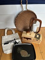 Photo showing full lot: large woven basket, wooden drawer box with two drawers, two wooden mushroom figurines, ceramic light switch cover, Massachusetts tote bag, vintage Couroc pineapple tray, wooden and glass lantern with candle