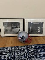 Framed photos and Patriots helmet displayed on wooden floor, showing the lot's main items
