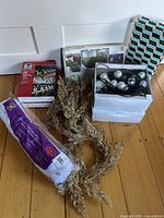 Photo showing assorted boxed light sets, light clips, gold garland, and advent calendar box on wooden floor.