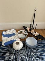 Complete lot of coastal beach decor items arranged on hardwood floor against beige wall. Includes fabric runner, bowls, wooden trough, candle sconce, seashells, and decorative piece.