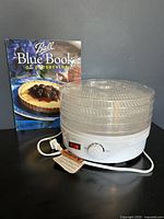 NutriChef food dehydrator with stacked trays and Ball Blue Book of Preserving cookbook in the background