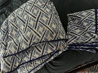 Folded comforter with geometric blue and white diamond pattern and dark blue edging placed on a dark surface