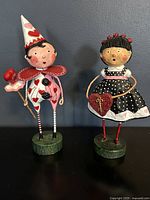 Two Lori Mitchell Valentine's Day figurines featuring a boy and a girl with heart motifs, standing on green bases.