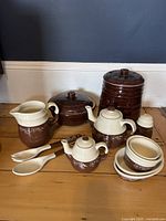 Full view of the Marcrest Daisy Dot cookie jar, Oxford Snowflower teapot and various stoneware pieces arranged on a wooden floor against a wall.