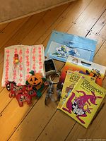 Photo showing vintage kids activity books with crossword puzzles, blue Smurfs folder, Halloween craft kit including pumpkin and two embroidered horses, and Pottery Barn Teen pillow sham with pink circular design.