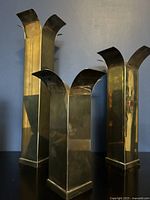 Set of three vintage brass candleholders in a dark setting, showing tall rectangular bodies and flared tops with spikes