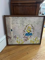 Framed original artwork showing girl in blue dress on flower-adorned swing hung from a tree with flowers below.