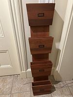 Front view of wooden wall-mounted filing station with four staggered compartments and metal label holders on each pocket.