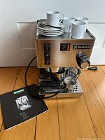 Front view of espresso machine with cups, saucers and spoons on top