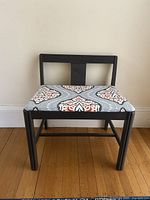 Front view of the small dark grey bench showing the upholstered seat with decorative pattern and simple backrest design.