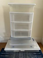 All five storage items stacked: four clear storage bins with white lids stacked below and above a three-drawer white-framed storage container in the center.