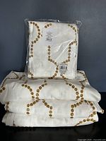 Four curtain panels shown folded; one panel is packaged, three are folded and opened; white panels with gold geometric dot pattern visible