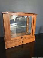 Front view of oak and glass display cabinet with drawer beneath glass front.