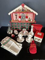 Wide shot of all items in the Christmas lot including the handmade wooden Advent calendar with drawers, ceramic candleholders, red cookie cutters, vintage napkins, ornaments, tin, and the vase on a black table against a dark wall.