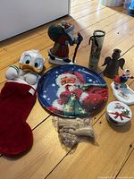 Overall lot view showing cast iron Santa doorstop, Donald Duck stocking, Santa tray, candleholders, trinket box, glitter candle, plastic nativity, and small holiday figurines arranged on the floor