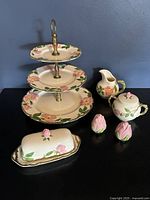 Full set view including tiered stand, creamer, sugar bowl, butter dish, salt and pepper shakers on black surface with blue background.