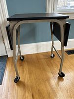 Photo of vintage typewriter table showing metal legs with caster wheels on hardwood floor against a light blue wall.