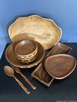 Full set of vintage wooden serving pieces including monkeypod platter, Baribocraft salad bowl and small bowls with dot inlays, rectangular divided tray, egg-shaped Akta Teak plate, and carved wooden fork and spoon.