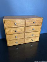 Front view of the wooden storage box showing all 8 drawers closed, the wood grain pattern and silver knobs.