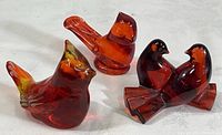 Four glass birds arranged on a white surface showing varying colors and styles, including deep ruby glass doves and hand-painted birds.