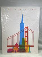 Front view of canvas print wrapped in plastic showing colorful silhouette art of San Francisco landmarks including the Golden Gate Bridge and TransAmerica Building with 'SAN FRANCISCO' text at top.