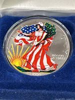 Close-up of colorized obverse side of the silver coin showing Lady Liberty with American flag, sun rising, and 'In God We Trust' text, year 2000 at bottom.