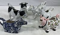 Group photo of six animal-shaped ceramic creamers: five cows and one goat in different designs and colors