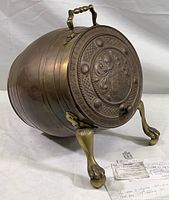 Side angle view showing round brass coal box on lion's paw feet with hinged lid and shaped carrying handle. Documents included in front.