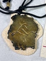 Close-up of the front of the polymer clay petroglyph pendant, showing the textured gold-toned carved design on a lighter base.