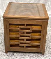 Front view of the wooden side table showing Asian style mid century modern design with geometric fretwork over fabric panels.