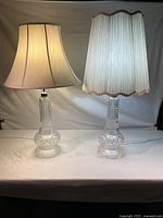 Pair of two clear glass table lamps with different fabric lampshades on a table against a white backdrop