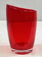 Front and side view of a smooth, cherry red glass vase with a clear glass base, showing the modern design and shape.