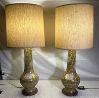Pair of vintage mid-century modern table lamps with porcelain bases decorated with Asian chrysanthemum motifs in brown tones, and beige fabric cylindrical shades, standing side by side and lit.