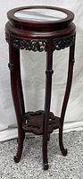 Full view of the tall dark wooden plant stand with a round marble top and carved apron and bottom shelf.
