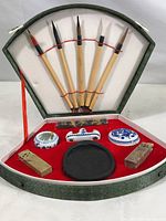 Five calligraphy brushes secured with red elastic bands inside a fan-shaped case.