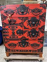 Front view of a red Japanese Tansu chest showing detailed black ironwork on multiple drawers and cabinet door, with two keys hanging.