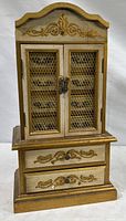 Front view of vintage wooden jewelry chest with decorative gold accents and double wire mesh doors.