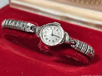 Vintage ladies wristwatch displayed in its red velvet presentation case, showing the full watch with band.