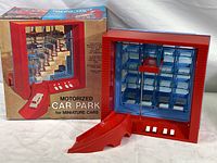 Vintage red plastic motorized car park toy displayed alongside original box with marketing graphics and text.