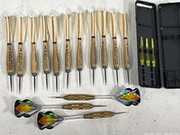 Eleven vintage wooden Widdy darts with feather flights, three Accudarts with reflective flights, three yellow extra dart stems in a black plastic carrying case on white surface.