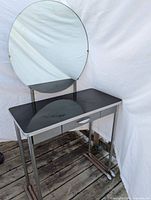Front angle view of the Art Deco vanity showing the large circular mirror, black tabletop, and metal frame with foot supports.