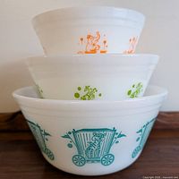 Stacked three Fire King nesting bowls showing circus designs in blue, green and orange.